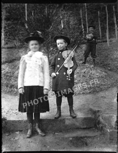 Un petit garçon jouant du violon, photographié au côté d'une jeune fille dans le jardin.